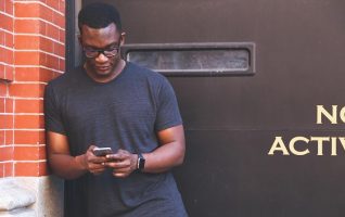man leaning against wall, texting