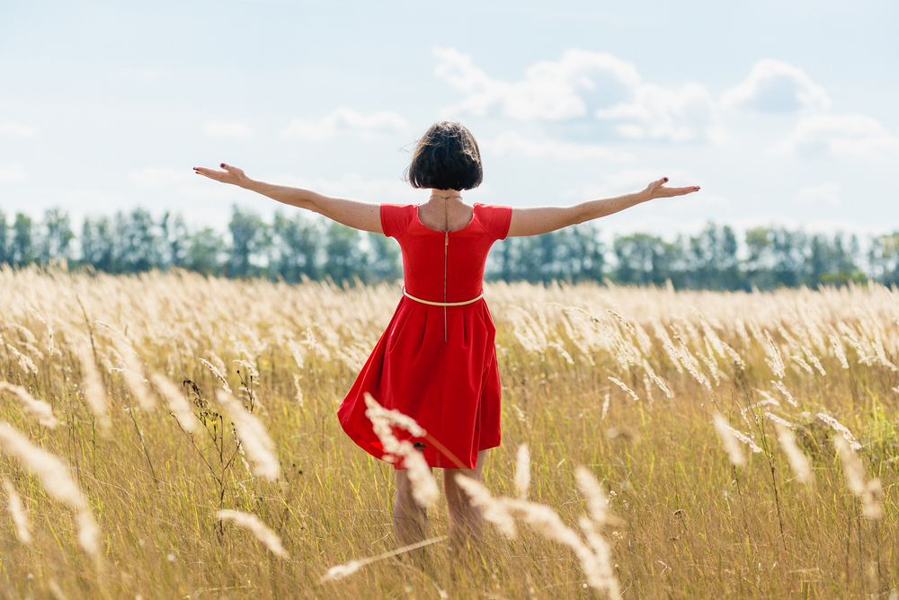 woman in red dress standing in meadow with arms outstretched