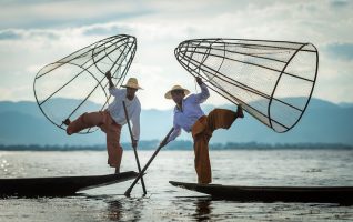 two asian fishermen balancing on their boats