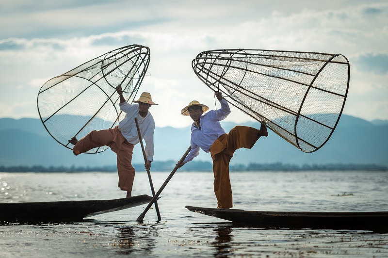 two asian fishermen balancing on their boats