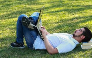 man lying down on the grass outside using laptop