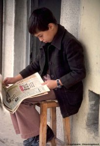 boy leaning over reading a newspaper on his lap