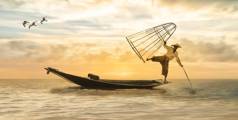 man balancing on edge of his fishing boat